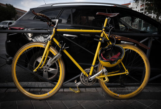 Yellow vintage bicycle and helmet parked next to a black car