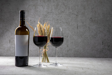 Rotweinflasche mit Etikette mit zwei gefüllten Weingläsern  mit Rotwein auf Betonwandhintergrund. Weingläser halb voll mit teuren Wein 