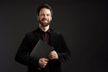 Bearded happy man in black jacket smiling while posing with laptop