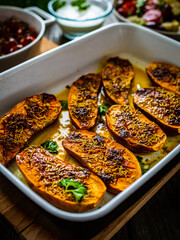 Roasted sweet potatoes  in cooking pan and vegetables on wooden table
