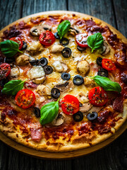 Pizza with white mushrooms, ham, tomatoes, olives, parmesan and mozzarella on wooden background
