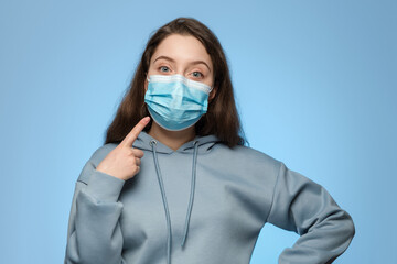 Woman is wearing a medical mask and points her finger at it. The girl shows that you have to wear a medical mask.