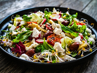 Fresh vegetable salad - feta cheese, tomatoes, radish, artichokes , lettuce, black olives and sprouts on wooden table

