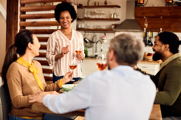 Happy black woman holding a toast while having lunch with friends at dining table.