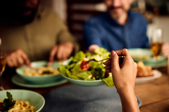 Close-up Of Black Woman Eating Salad While Having Lunch With Friends At Dining Table.