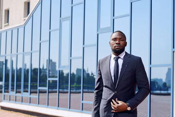 Young African business professional in elegant suit standing in front of camera against exterior of modern building in urban environment