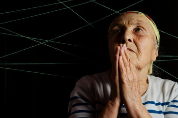 Elderly woman in prayer on a dark background. An old woman in prayer. Grandmother's wrinkled hands...