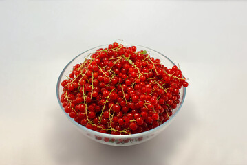 Large bowl of red currant with sprigs on a white background.