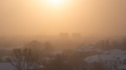 Obraz premium Top view of snowy roofs of houses in winter during a blizzard at sunset. Orange city defocused background