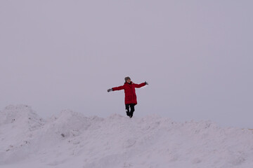 Naklejka na ściany i meble Smiling girl in a red jacket is having fun on a snowy mountain in winter. Childhood concept
