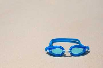 Blue swimming goggles lie on the white sea sand on the beach. Blue swimming gear on the sand. The concept of sports. Swimming goggles on a snow-white beach, protect your eyes from water ingress
