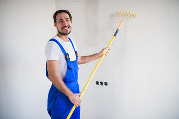 Man paints the wall with a roller, smiles and looks at the camera