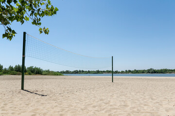 Volleyball net on river beach with white sand, bright summer day. Healthy lifestyle, outdoor activities
