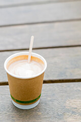 Recyclable coffee cup with a stiring stick standing on wooden surface, tasty caffeine drink in paper single use cup isolated on the bench, new eco friendly approach for takeaway drinks