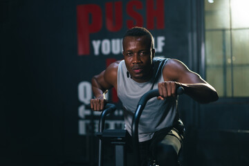 African ethnicity man listening music while using spinning bike on cardio machine in fitness gym