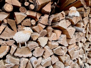A toy white lambs lies snugly on a stack of firewood. A beautiful lambs hid in the wood. A lambs...