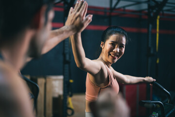 Asian female and Caucasian male athletes or sport people giving high five together after successed training on stationary bicycle. Health care and fitness in gym concept