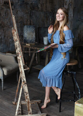 Young beautiful artist in blue dress with easel and palette