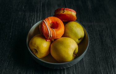 yellow-green apples and a couple of ornamental and pink donuts are in a plate on the table .. dark background. background with food. fresh juicy apples. delicious sweet donut.