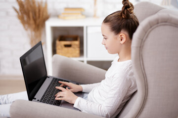 Naklejka premium childhood and online education concept - cute girl using laptop in bright living room