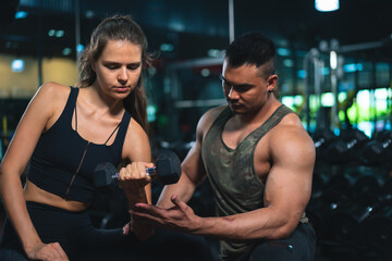 Caucasian young woman in sportswear lifting dumbbell  with trainer care for safety in fitness club or gym.