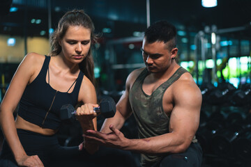 Naklejka premium Caucasian young woman in sportswear lifting dumbbell with trainer care for safety in fitness club or gym.