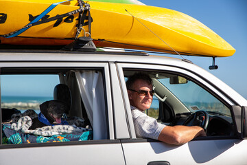 A male tourist pauses to take in the seaside view. He is driving a campervan with kayaks on the...