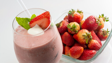 delicious strawberry smoothie in the foreground decorated with good herb and supermarket transparent plastic container full of strawberries in the background on white background