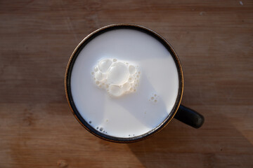 Glass of milk standing on old wooden table. Black glass with white milk. Black glass with white milk on the table