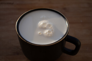 Glass of milk standing on old wooden table. Black glass with white milk. Black glass with white milk on the table