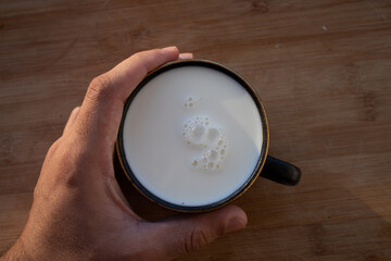Glass of milk standing on old wooden table. Black glass with white milk. Black glass with white milk on the table