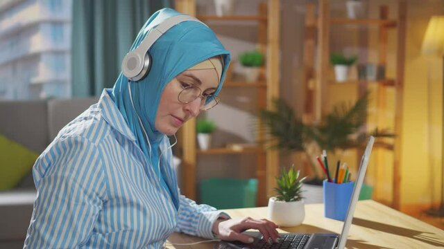 Portrait young muslim freelancer in a national headscarf works at a laptop sitting in the living room