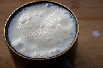 Glass of milk standing on old wooden table. Black glass with white milk. Black glass with white milk on the table