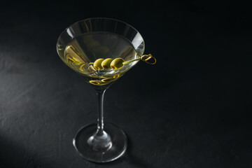 Glass of classic dry martini cocktail with olives on dark stone table against a black background.