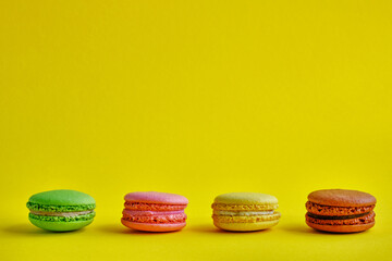 Four multi-colored appetizing macaroons lie on a yellow surface