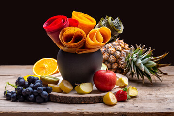 Multicolored fruit marshmallow rolled into rolls on a black background and fruits 