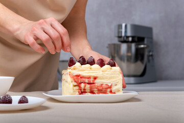 Confectioner woman decorates cake with raspberries. Vanilla cream cake with berry filling.