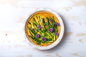 Green asparagus, sweet peas Tart with edible chives flowers or blossoms. Seasonal spring dinner, overhead view.