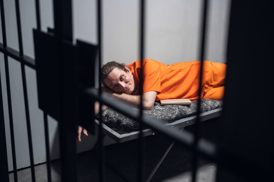 Lights out in prison. A convict in an orange robe rests on a bunk in a cell with a book.