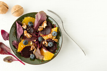 Fototapeta na wymiar vegetarian salad with baked beets and orange in a green ceramic plate on a light table, vegetarian food concept
