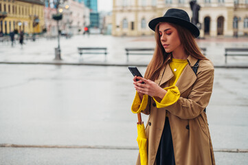 Woman with yellow umbrella using a smartphone