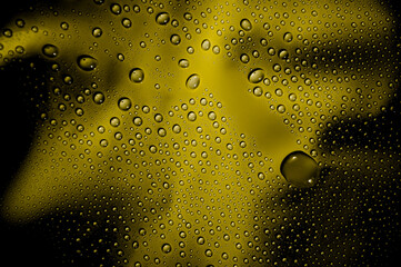 Water drops on glass. Yellow smoke behind wet glass with water droplets on the surface. Abstract yellow background with drops and shadows.