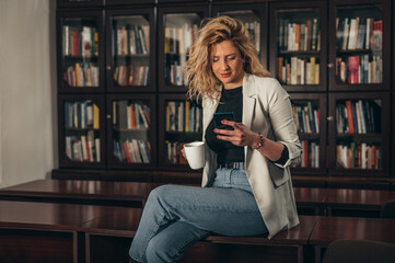 Woman drinking coffee and using smartphone in the office