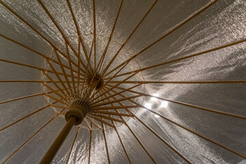 Spread open translucent fabric umbrella backlighted by light rays forming a geometric design