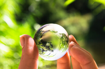 Crystal globe in the hand of a man against a background of green foliage. Earth protection concept. Earth Day