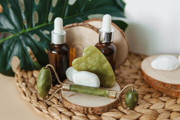 Jade Gua sha scraper and roller face massager, bottles of cosmetic serum for the face on wooden...