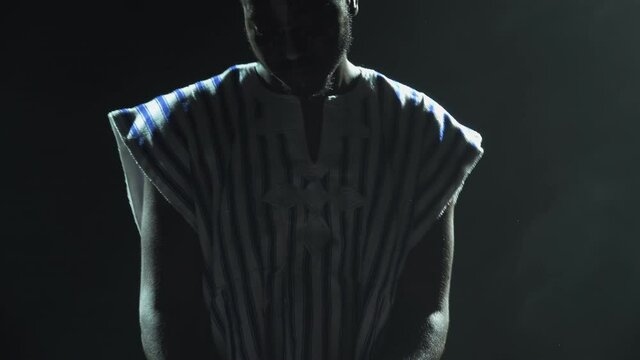 Silhouette of african american man playing piano synthesizer on stage in dark smoky studio. Black musician with a white ethnic pattern on his face performs against the background of lights. Close up.