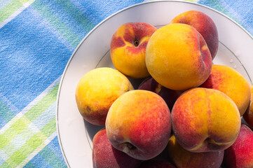 Delicious and flavorful fresh peaches on a white plate on a table with blue tablecloth outdoors