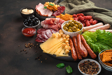 Meat and cheese snacks with salad and olives on a brown background.