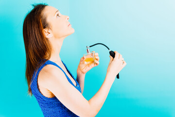 Smiling young beautiful woman spraying perfume her neck with blue background. flirtatious woman concept, personal care